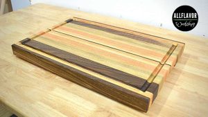 Finished DIY edge grain cutting board made from walnut, ash, and beech with juice groove and handles.