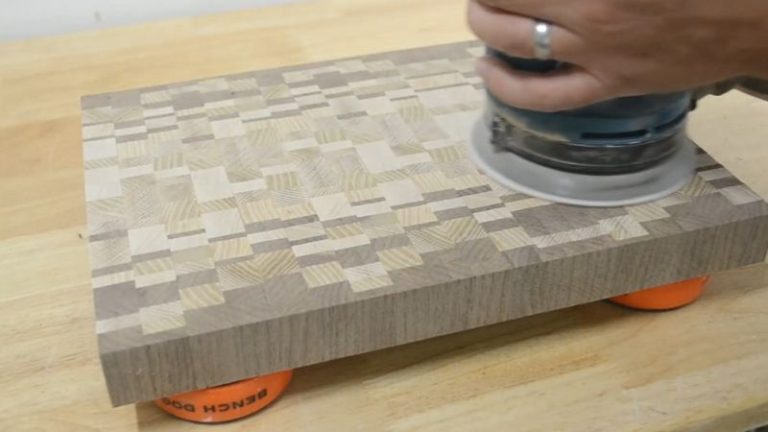 Sanding the surface of an end grain cutting board with an orbital sander to remove cut marks.