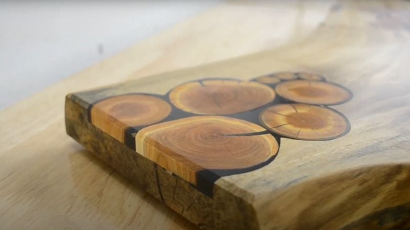Close-up of walnut cutting board surface showing cherry wood inlays and black epoxy fill.