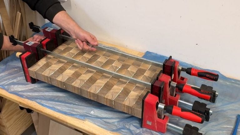 End grain cutting board panel in parallel clamps with the blocks aligned tightly and glue squeeze-out visible.