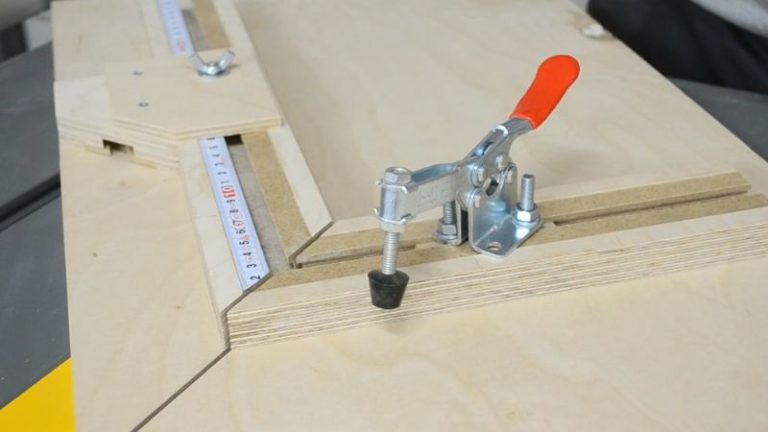 Hold-down clamp mounted in the fence T-track, pressing a frame piece against the picture frame jig fence.