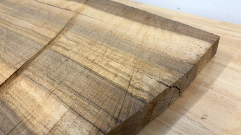 Rough walnut slab with end cracks, surface cracks, and slight cupping before trimming.