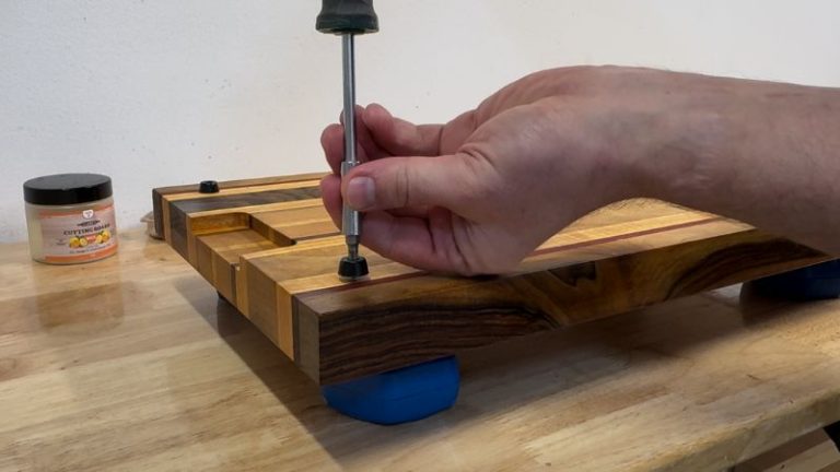 Reinstalling rubber feet on a refinished cutting board using screws on the underside.