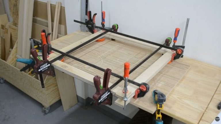 Corner clamps and long clamps holding a plywood frame square during glue-up.