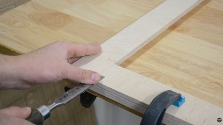 Cleaning dried glue from plywood frame joints with a chisel after glue-up.