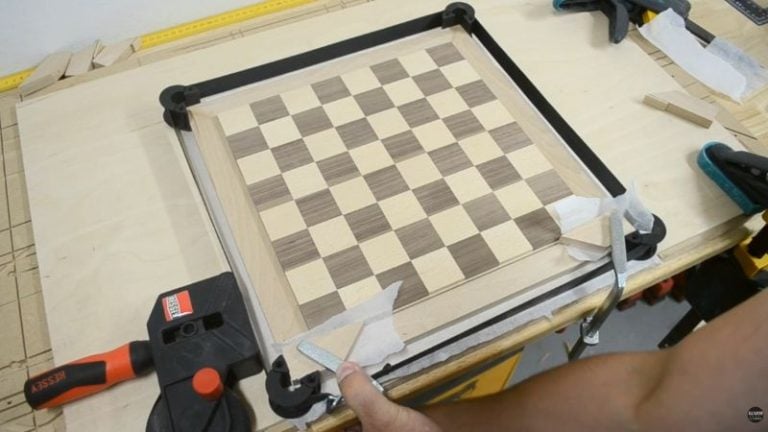 Gluing and clamping a beech chessboard frame with a strap clamp to close miter corners without gaps.
