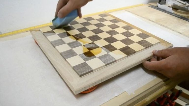 Applying Belinka oil to a wooden chess board with wax paper underneath to protect the work surface from excess oil.