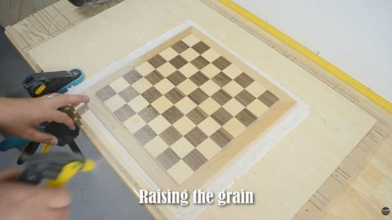 Spraying water on a sanded wooden chess board to raise the grain before the final sanding pass.