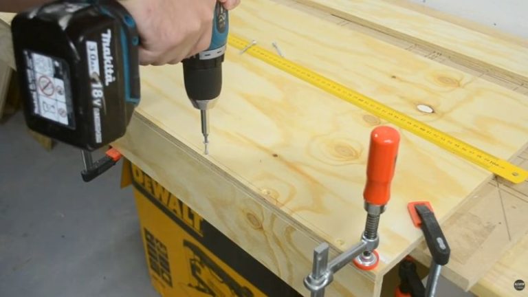 Clamping the back bottom support to the base of a lumber cart and fastening it with screws from the underside after predrilling and countersinking.