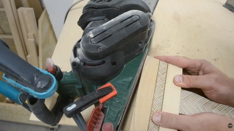 Sanding and shaping the wooden mallet head to final form using an orbital sander and belt sander, smoothing faces and breaking edges.