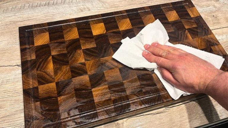 Drying a wooden cutting board with a towel after washing and rinsing off the soap.